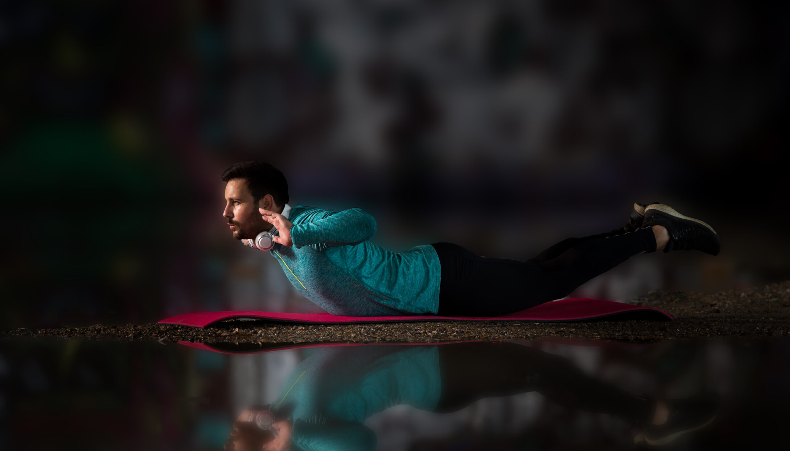 Attractive man in sportswear doing back extension on yoga mat beside pond with reflection in water